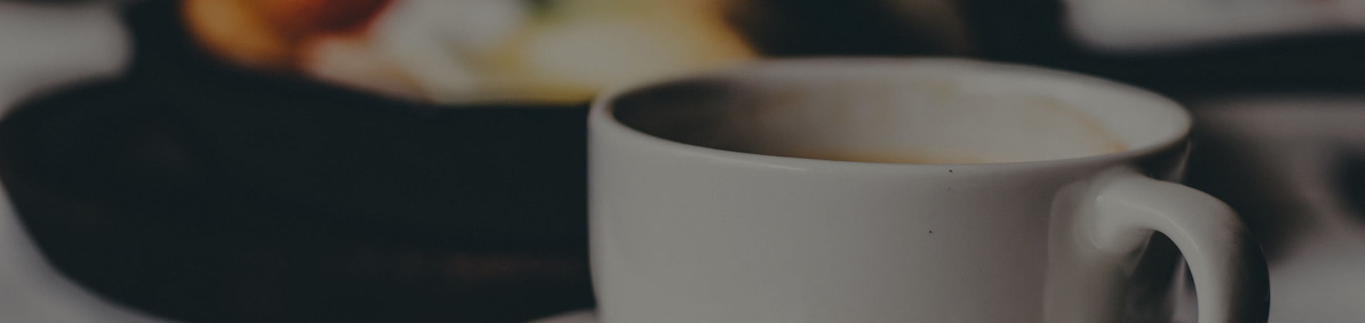 Una taza de café y en segundo plano el resto del desayuno